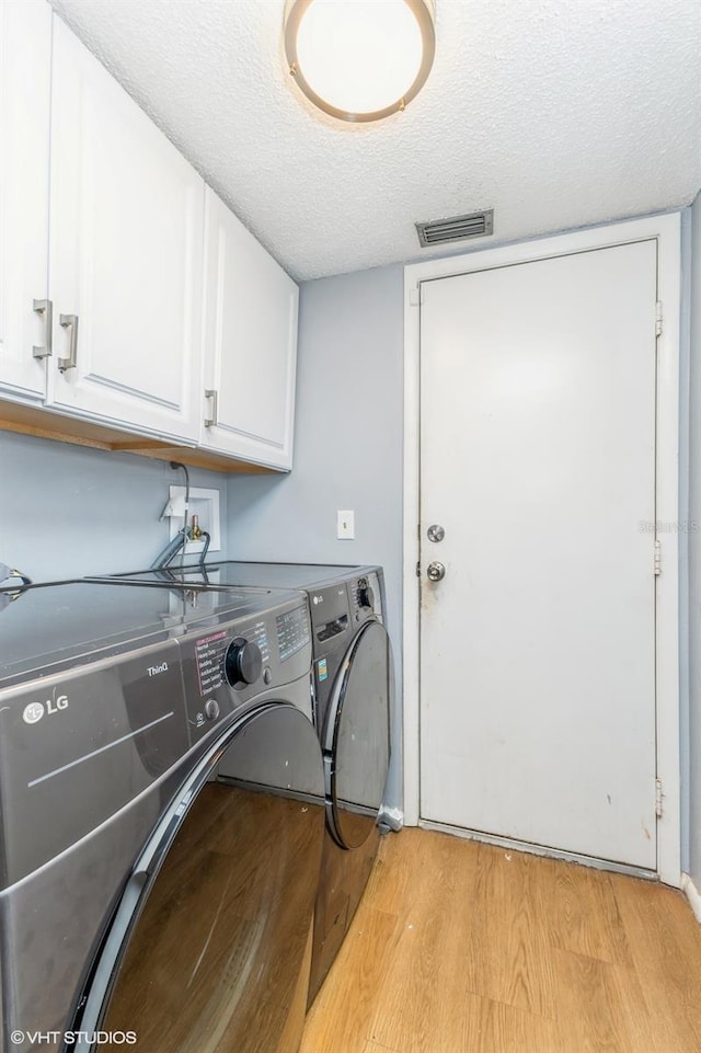 laundry room with visible vents, washer and clothes dryer, a textured ceiling, cabinet space, and light wood-type flooring