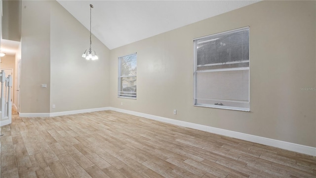 unfurnished room with high vaulted ceiling, light hardwood / wood-style floors, and an inviting chandelier