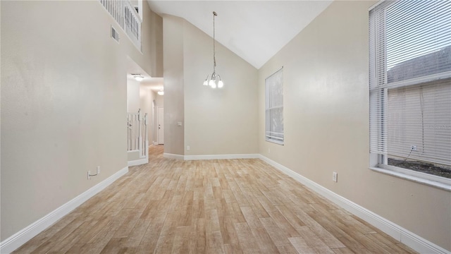 spare room with high vaulted ceiling, a chandelier, and light wood-type flooring