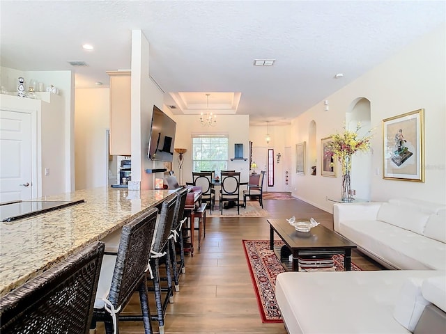 living room with hardwood / wood-style flooring, a raised ceiling, and an inviting chandelier