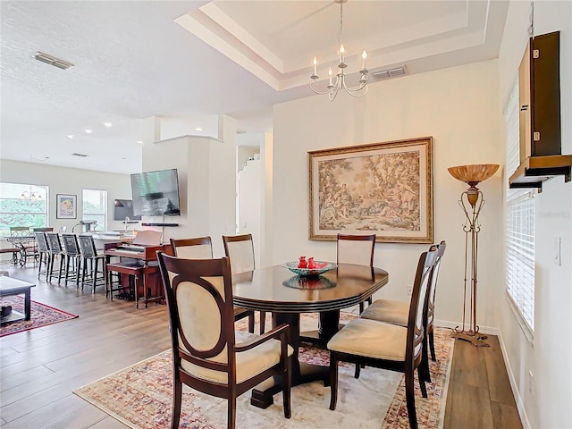 dining area with a raised ceiling, light hardwood / wood-style flooring, and a wealth of natural light