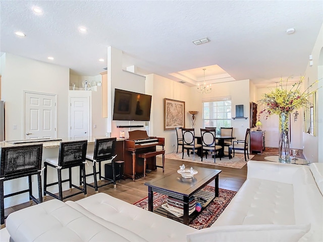 living room with a textured ceiling, hardwood / wood-style floors, a chandelier, and a tray ceiling