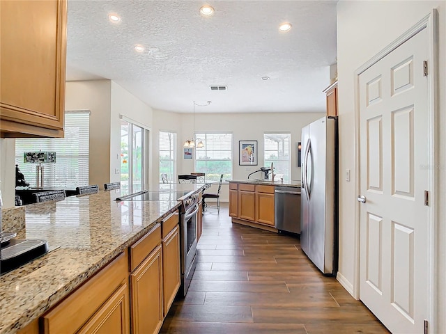 kitchen with stainless steel appliances, light stone counters, hanging light fixtures, dark hardwood / wood-style floors, and a textured ceiling