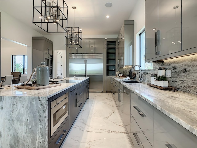 kitchen with decorative backsplash, built in appliances, hanging light fixtures, gray cabinetry, and sink