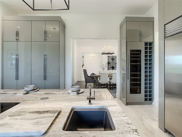 kitchen featuring built in fridge, sink, light stone counters, a notable chandelier, and gray cabinets