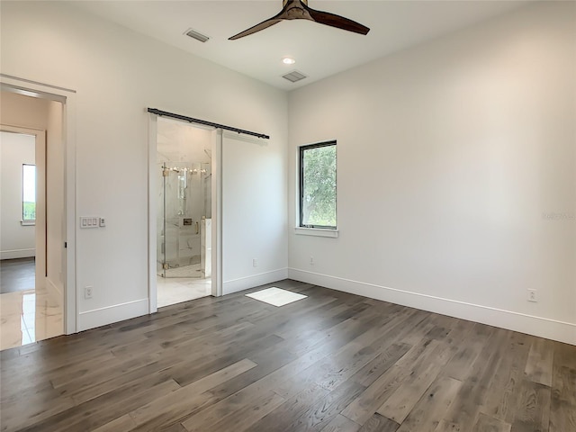 unfurnished bedroom with ceiling fan, multiple windows, dark wood-type flooring, a barn door, and ensuite bathroom