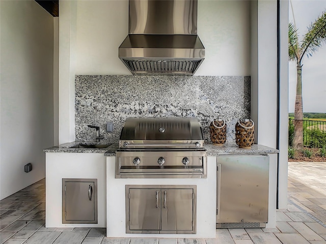 kitchen with stone counters, wall chimney exhaust hood, decorative backsplash, and refrigerator