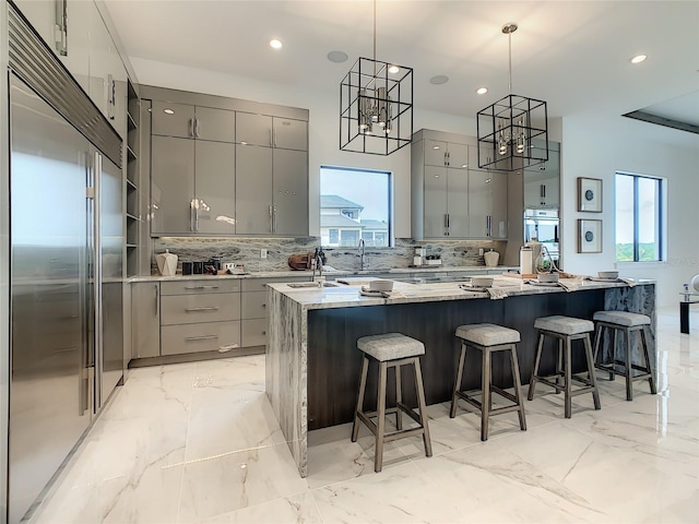 kitchen featuring hanging light fixtures, gray cabinetry, a large island, light stone counters, and stainless steel appliances