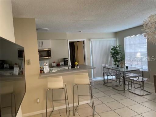1073 S Hiawassee Rd Unit 1018, Orlando, FL 32835 - kitchen featuring a textured ceiling, stainless steel microwave, white cabinetry, baseboards, and a peninsula
