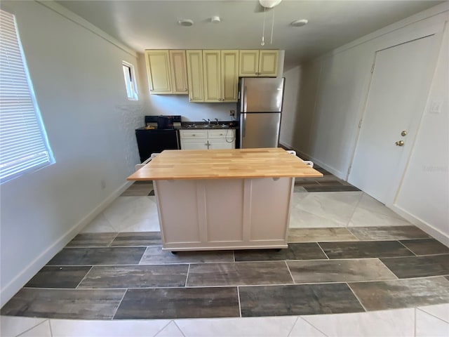 kitchen with a kitchen island, tile patterned floors, stainless steel refrigerator, butcher block counters, and cream cabinetry