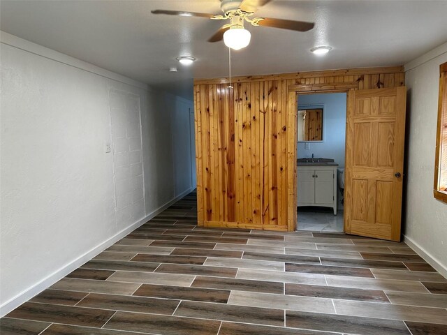 unfurnished bedroom with ceiling fan, wooden walls, and ensuite bathroom