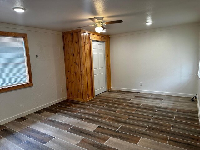 unfurnished bedroom featuring wood walls, a closet, ceiling fan, and dark wood-type flooring