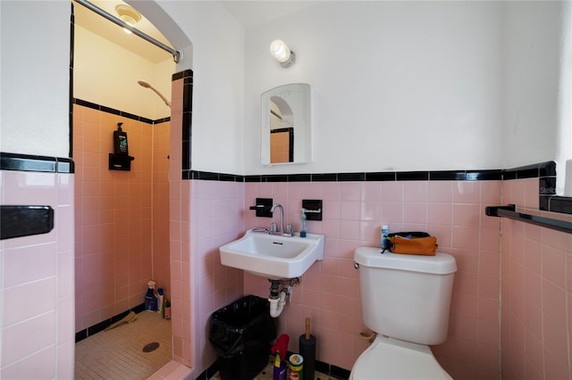 bathroom with tile walls, backsplash, a tile shower, and toilet