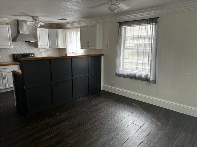 kitchen with dark hardwood / wood-style flooring, ceiling fan, white cabinetry, stove, and wall chimney range hood