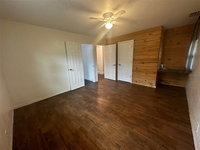 unfurnished bedroom featuring wood walls, ceiling fan, and dark hardwood / wood-style flooring