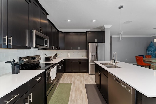 kitchen featuring decorative light fixtures, sink, backsplash, stainless steel appliances, and a center island with sink