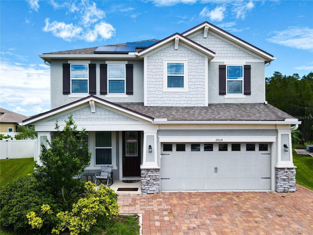 craftsman house featuring a porch, an attached garage, solar panels, roof with shingles, and decorative driveway