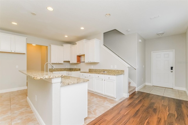 kitchen with white cabinets, light stone counters, light hardwood / wood-style flooring, and a kitchen island with sink