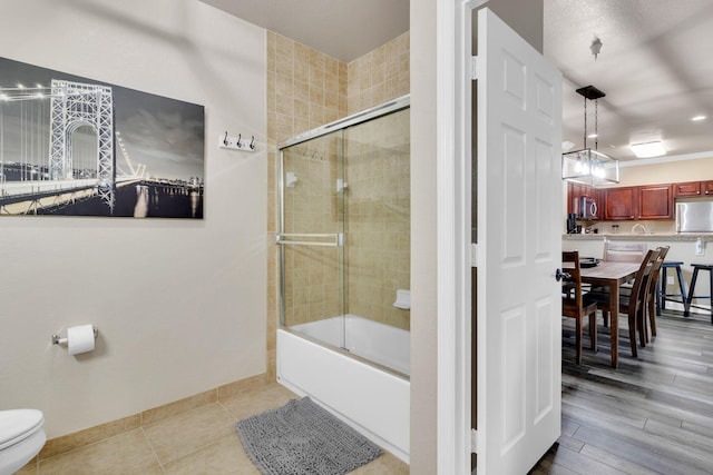 bathroom with combined bath / shower with glass door, toilet, and hardwood / wood-style flooring