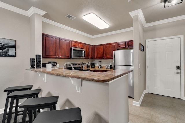 kitchen with light tile patterned floors, a kitchen bar, stainless steel appliances, and ornamental molding