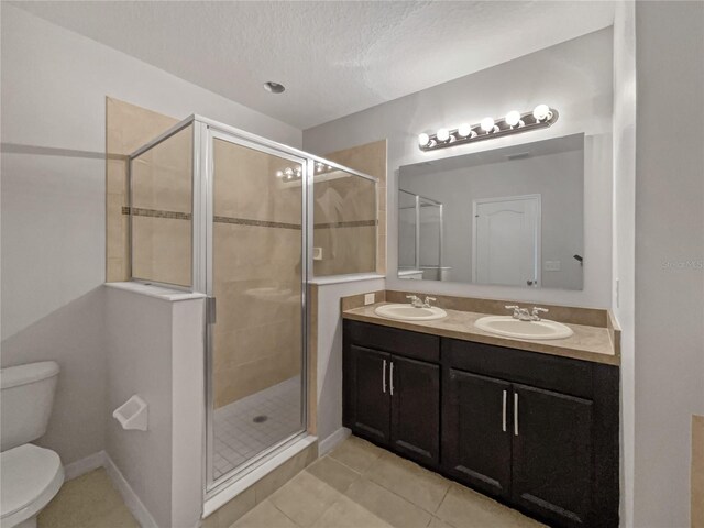 bathroom with a textured ceiling, a shower with door, toilet, double vanity, and tile patterned flooring