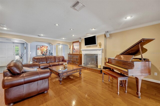 living room with a textured ceiling, decorative columns, light hardwood / wood-style flooring, and ornamental molding