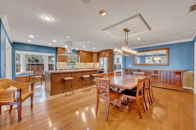 dining area featuring sink, light hardwood / wood-style flooring, washer / clothes dryer, crown molding, and a textured ceiling