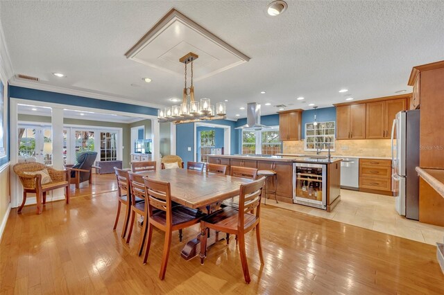 dining space featuring wine cooler, light hardwood / wood-style flooring, a healthy amount of sunlight, and a textured ceiling