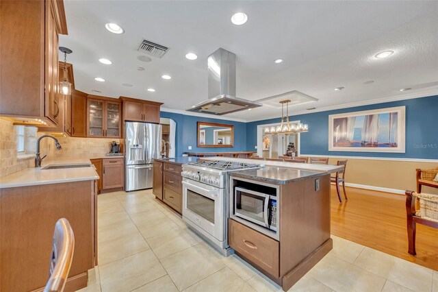 kitchen featuring island exhaust hood, stainless steel appliances, sink, pendant lighting, and a kitchen island