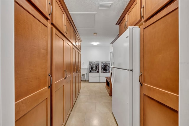 kitchen with a textured ceiling, white refrigerator, washing machine and dryer, and light tile patterned flooring