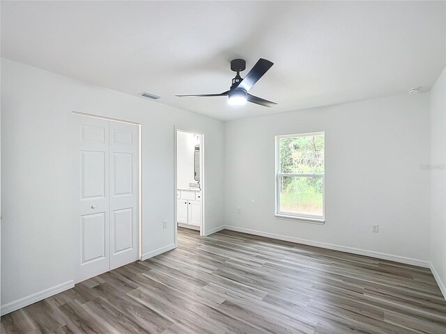 unfurnished bedroom featuring hardwood / wood-style flooring, ceiling fan, a closet, and ensuite bath