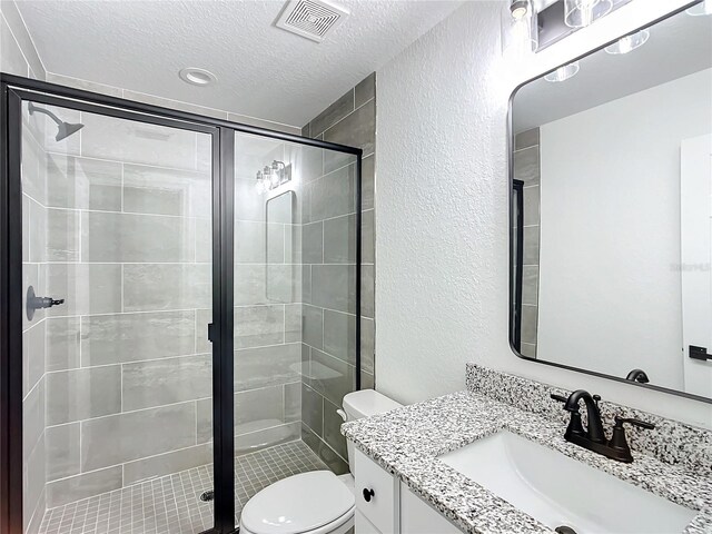 bathroom featuring toilet, vanity, a textured ceiling, and a shower with shower door