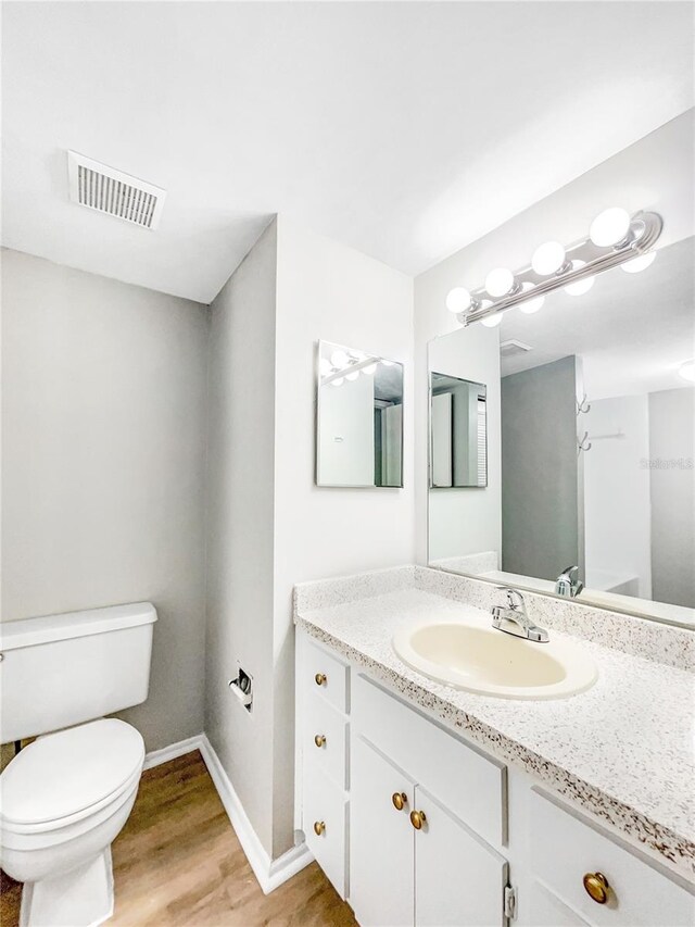 bathroom with toilet, vanity, and wood-type flooring