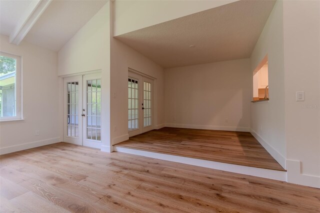 unfurnished room with high vaulted ceiling, light wood-type flooring, beamed ceiling, and french doors