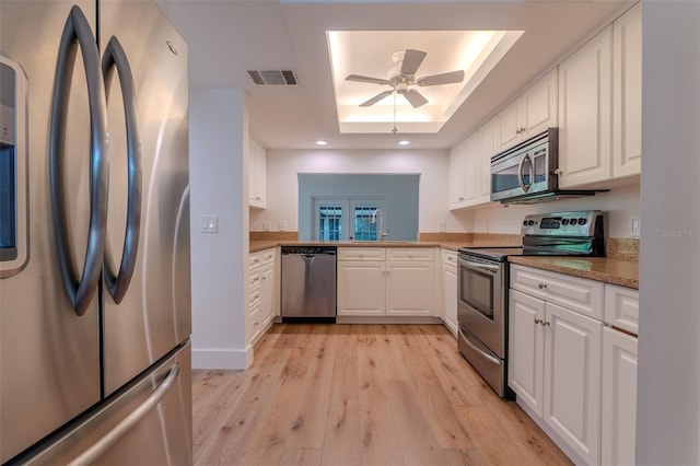 kitchen with appliances with stainless steel finishes, a raised ceiling, white cabinetry, and visible vents