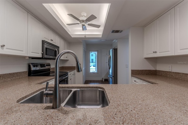 kitchen featuring ceiling fan, white cabinets, a raised ceiling, and stainless steel appliances