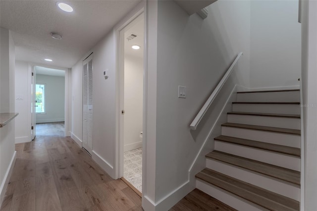 staircase with light hardwood / wood-style floors and a textured ceiling