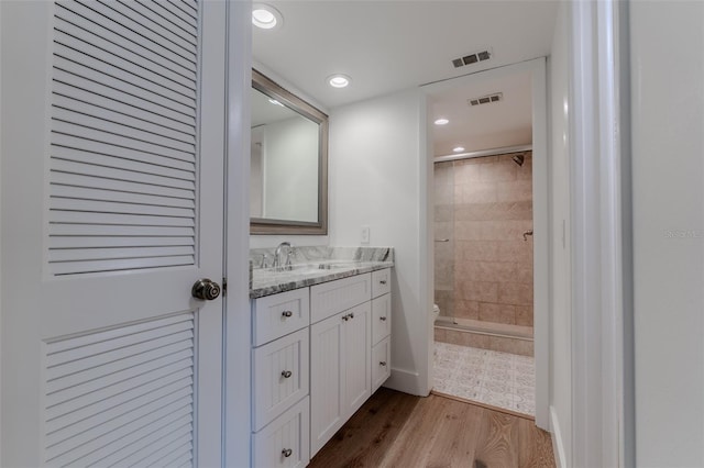 bathroom with toilet, vanity, tiled shower, and wood-type flooring