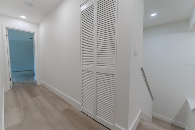 hall with an upstairs landing, baseboards, and light wood finished floors