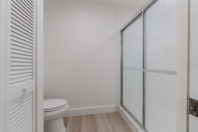 bathroom featuring hardwood / wood-style floors, toilet, and a shower with door