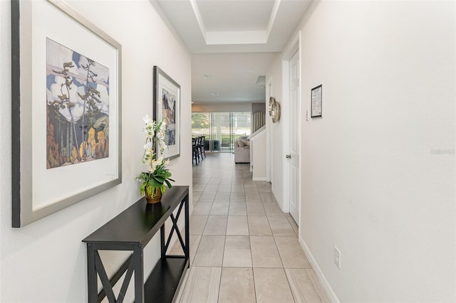 corridor featuring a tray ceiling and light tile patterned floors