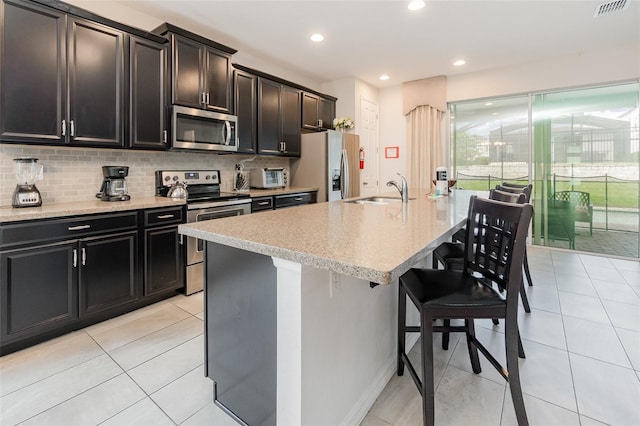 kitchen with sink, stainless steel appliances, light tile patterned floors, and a center island with sink