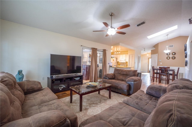 living room with lofted ceiling with skylight, a textured ceiling, ceiling fan, and hardwood / wood-style floors