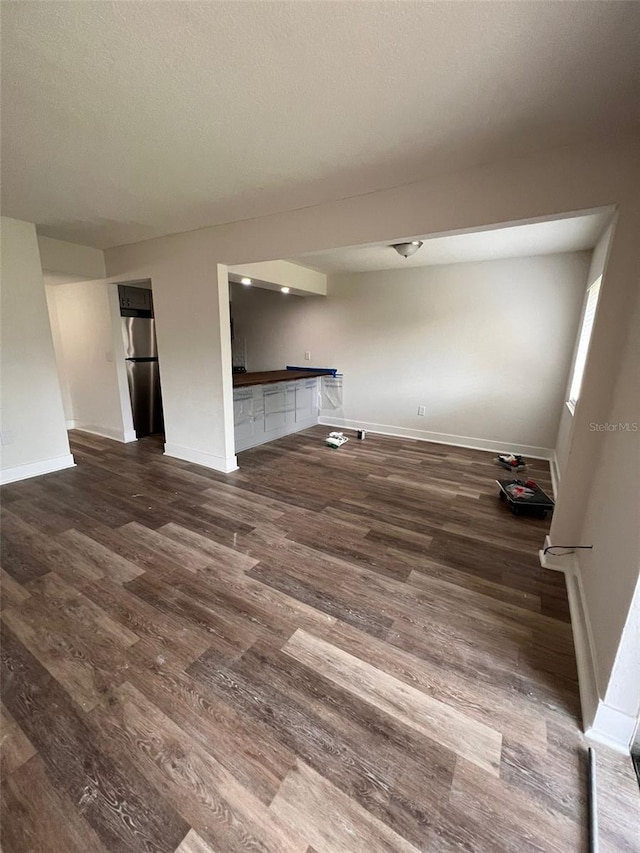 unfurnished living room featuring a textured ceiling, dark wood-type flooring, and baseboards