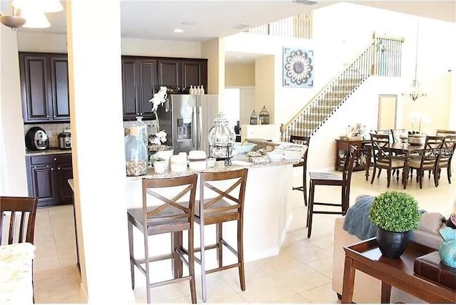 kitchen featuring a breakfast bar area, light stone countertops, stainless steel fridge, light tile patterned floors, and dark brown cabinetry