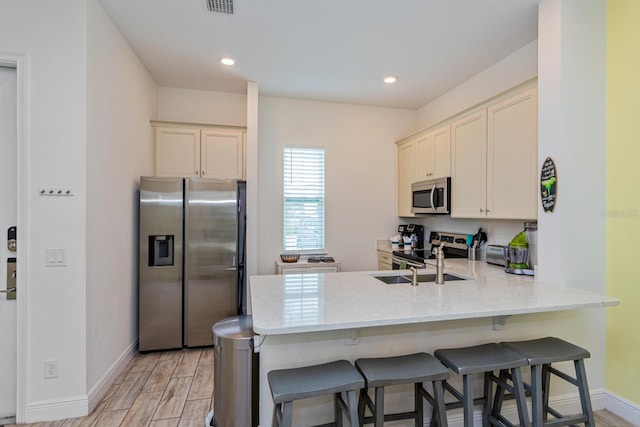 kitchen with kitchen peninsula, a kitchen breakfast bar, light wood-type flooring, sink, and stainless steel appliances