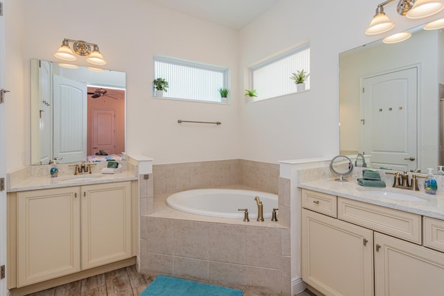 bathroom with vanity, wood-type flooring, tiled tub, and ceiling fan