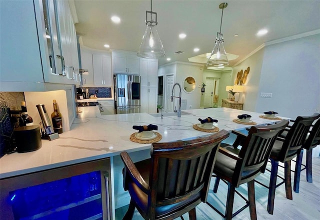 kitchen with crown molding, a peninsula, a sink, stainless steel refrigerator with ice dispenser, and pendant lighting