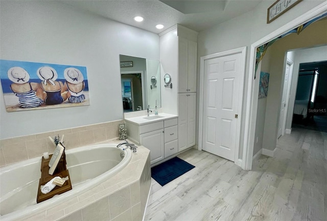 bathroom with baseboards, wood finished floors, vanity, a bath, and recessed lighting