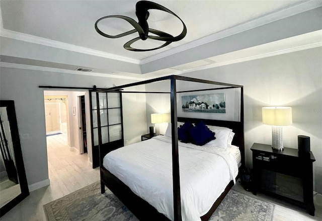 bedroom with a tray ceiling, crown molding, a barn door, wood finished floors, and baseboards